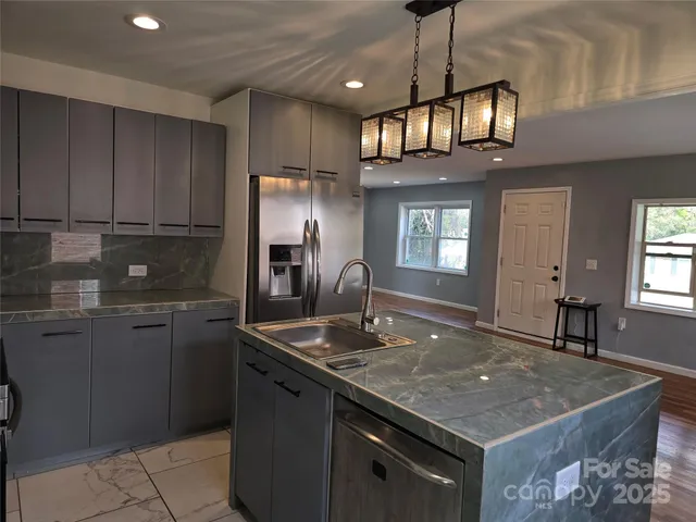 a kitchen with kitchen island granite countertop a sink a counter top space cabinets and stainless steel appliances