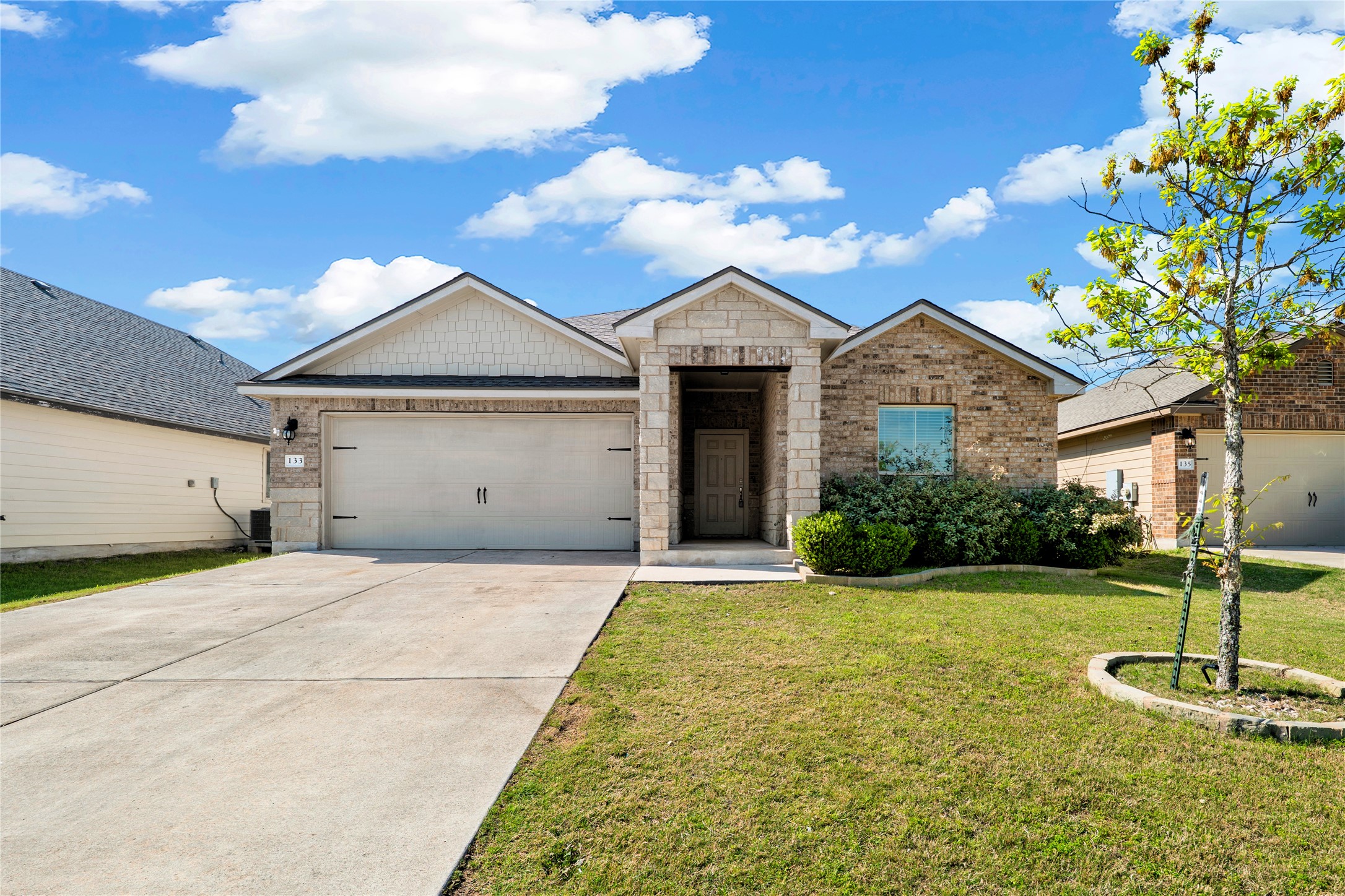 133 Beth Ann Loop Taylor, TX 76574 - Photo 27 of 30 View of front of house featuring driveway, a garage, a front lawn, brick siding, and stone siding