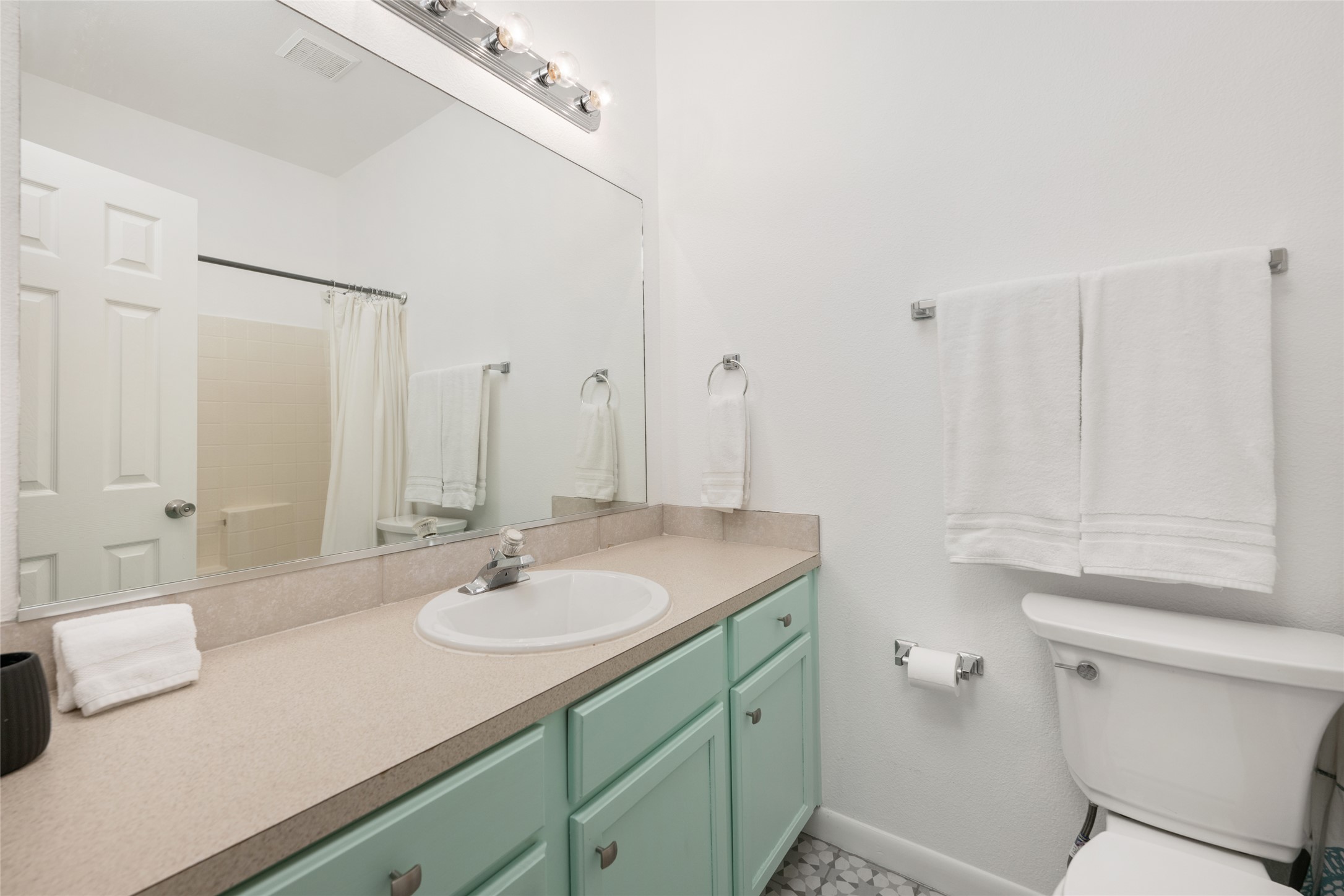 5613 Signal Point Austin, TX 78724 - Photo 15 of 21 Bathroom featuring a single vanity with a mint-colored cabinet base, a large wall-mounted mirror, overhead vanity lighting, and a built-in bathtub with shower