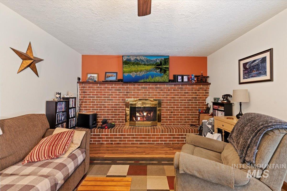 11650 Columbia Road Boise, ID 83709 - Photo 7 of 32 Living room featuring a fireplace, wood finished floors, a textured ceiling, and a ceiling fan