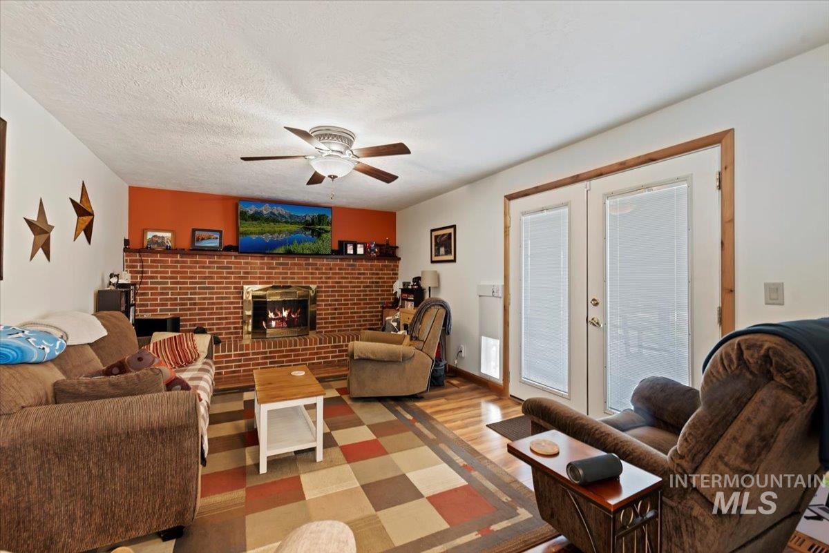 11650 Columbia Road Boise, ID 83709 - Photo 8 of 32 Living area with wood finished floors, a brick fireplace, a ceiling fan, french doors, and a textured ceiling