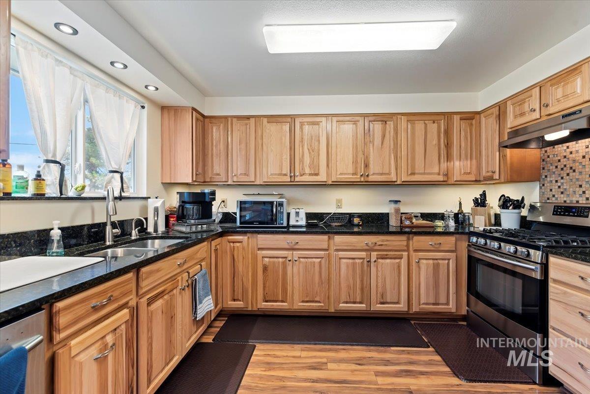 11650 Columbia Road Boise, ID 83709 - Photo 10 of 32 Kitchen with stainless steel appliances, dark stone countertops, under cabinet range hood, light wood-style floors, and recessed lighting