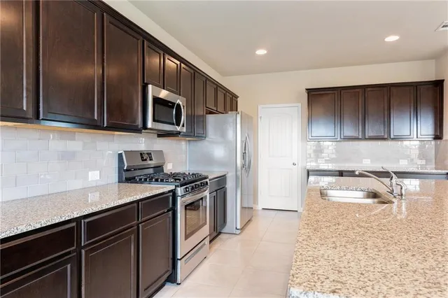 a kitchen with granite countertop wooden cabinets a stove top oven and stainless steel appliances