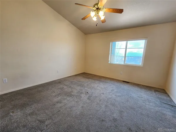 an empty room with a chandelier fan and windows
