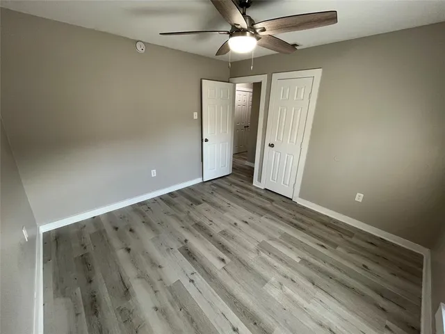 an empty room with wooden floor fan and windows