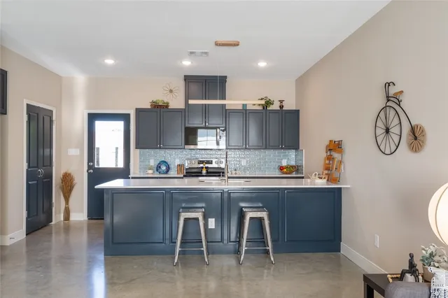 a kitchen with stainless steel appliances granite countertop a sink a stove a refrigerator cabinets and a dining table with wooden floor