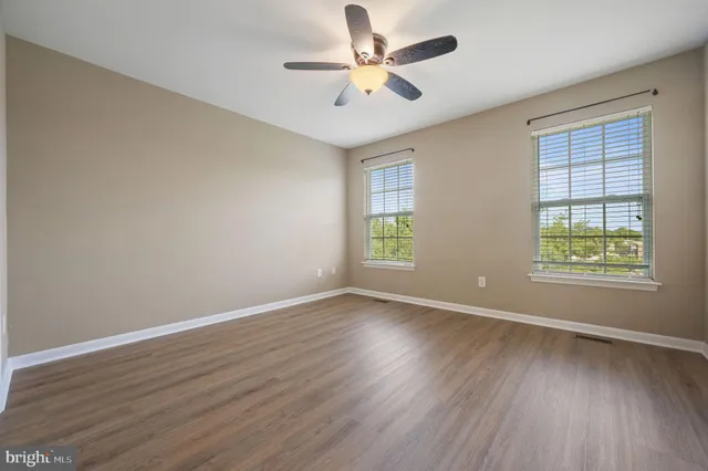an empty room with wooden floor ceiling fan and windows