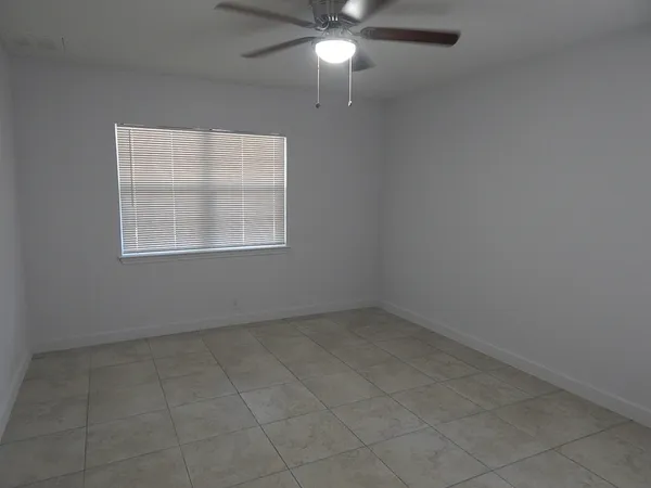 an empty room with chandelier fan and windows
