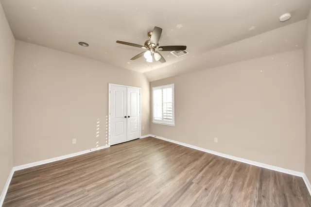 an empty room with wooden floor ceiling fan and windows