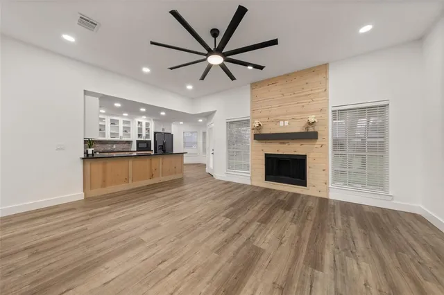an empty room with wooden floor a ceiling fan a fireplace and windows