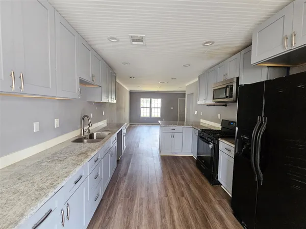 a large kitchen with granite countertop a stove top oven a sink dishwasher and white cabinets with wooden floor