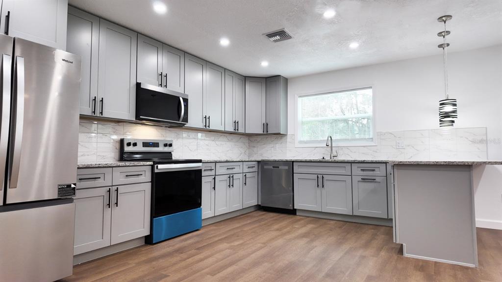 2607 Northeast 140th Street Citra, FL 32113 - Photo 11 of 36 a kitchen with stainless steel appliances granite countertop a stove top oven a sink dishwasher a refrigerator and a microwave oven with wooden floor