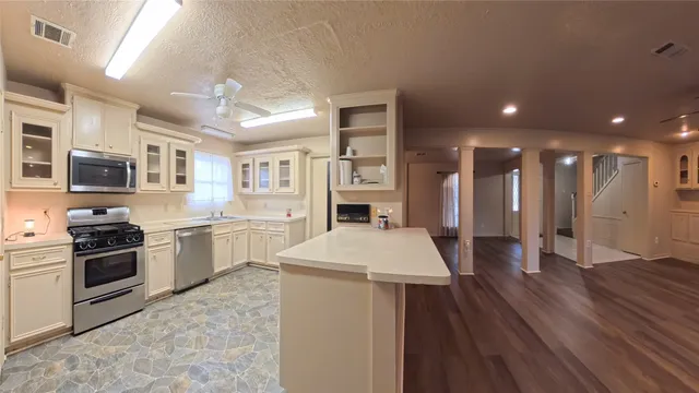 a kitchen with stainless steel appliances granite countertop a refrigerator a stove oven a sink dishwasher and white cabinets with wooden floor