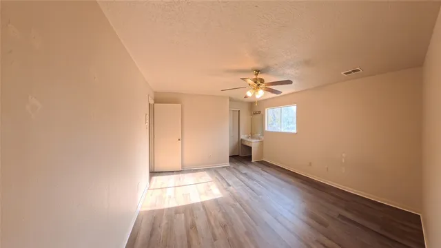an empty room with wooden floor chandelier fan and windows
