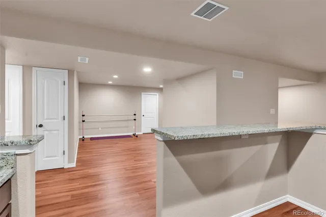 a view of an empty room with wooden floor and a kitchen