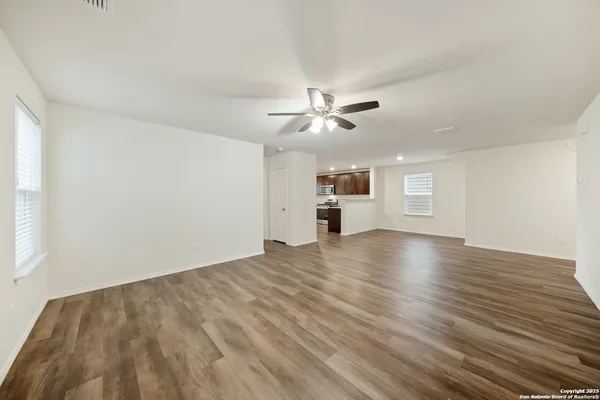 an empty room with wooden floor ceiling fan and windows