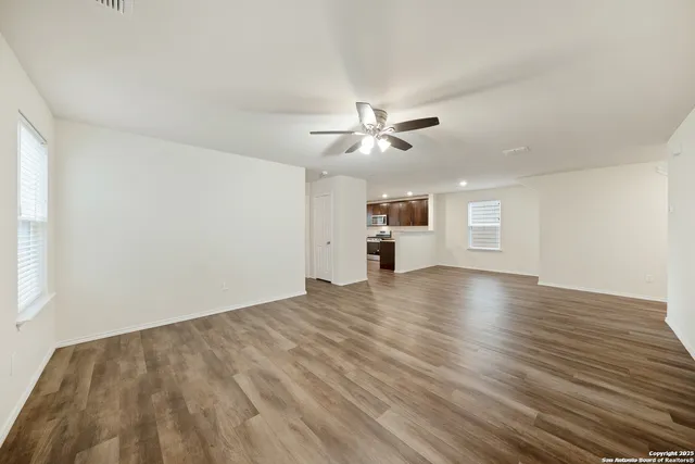 an empty room with wooden floor ceiling fan and windows