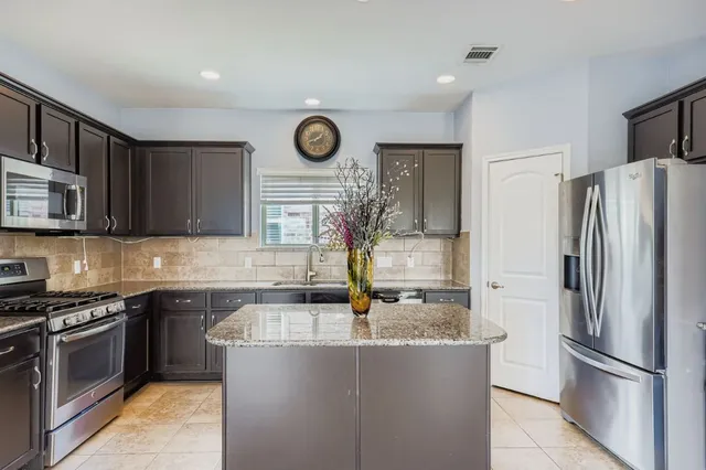 a kitchen with stainless steel appliances granite countertop a sink a stove a refrigerator and a microwave