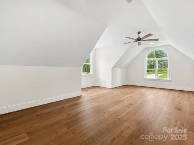 an empty room with wooden floor chandelier fan and windows