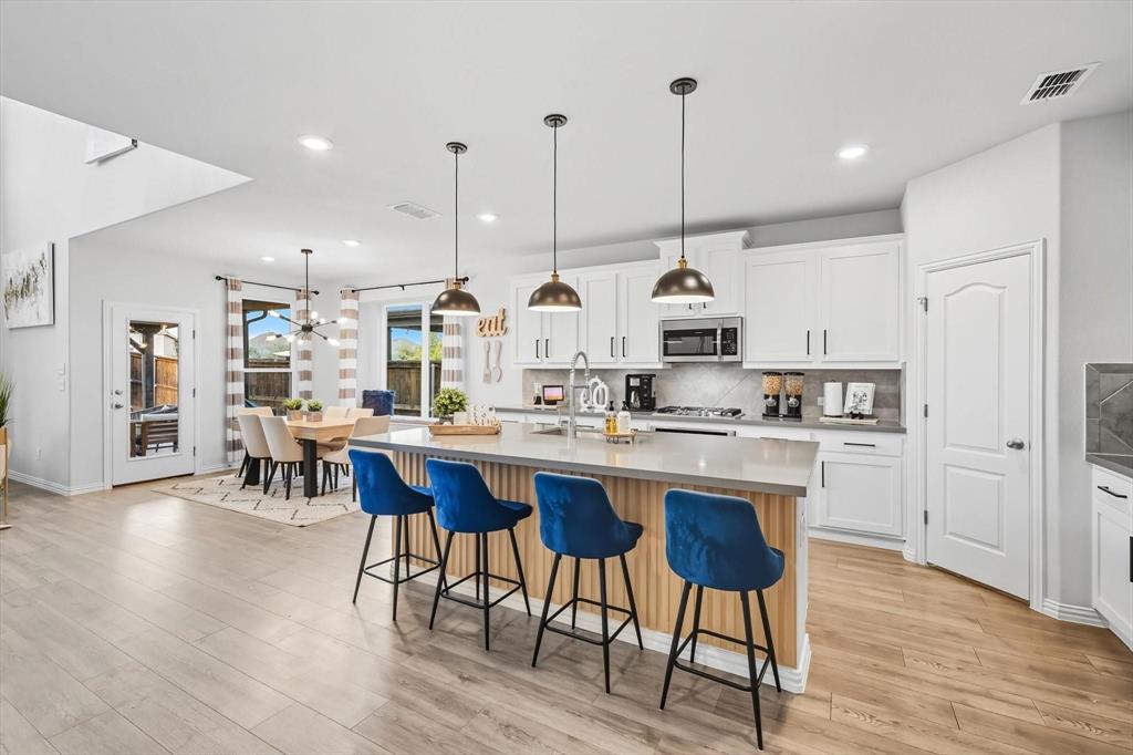1724 Wassel Road Fort Worth, TX 76052 - Photo 6 of 24 Open-concept kitchen featuring an island with pendant lighting, white cabinetry, integrated stainless steel appliances, and wood-finish flooring