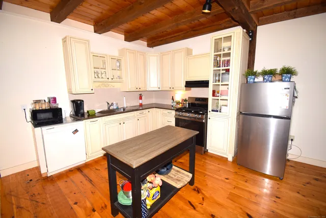 a kitchen with granite countertop a refrigerator a stove a sink and white cabinets with wooden floor