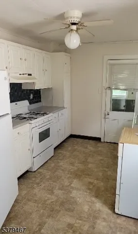 a kitchen with granite countertop a stove a sink and white cabinets