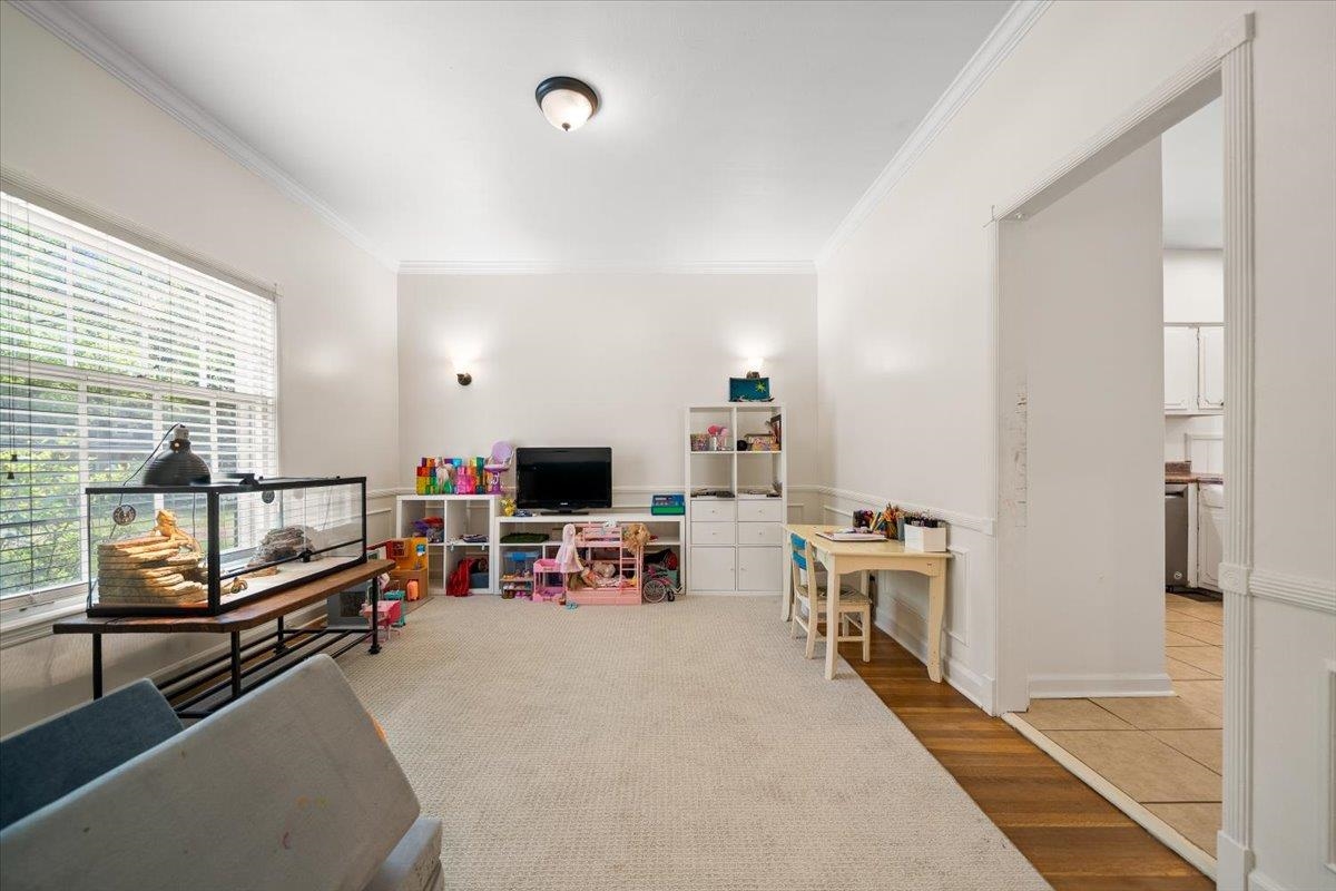 1273 Brookfield Road Memphis, TN 38119 - Photo 10 of 40 Spacious room featuring a large window with blinds, overhead lighting, two sconces, and a wide entryway showcasing wood-finish flooring; currently being used as playroom