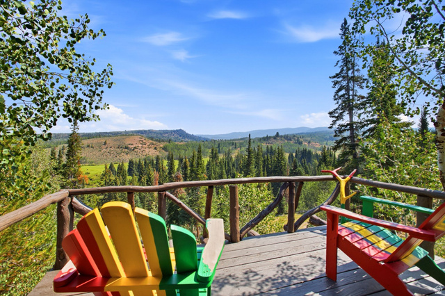 1663 Lancer Lane Evanston, UT 82930 - Photo 87 of 101 Expansive wood-plank deck with a rustic branch railing, surrounded by mature trees, overlooking a distant forested landscape
