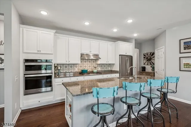 a kitchen with stainless steel appliances granite countertop a stove top oven a refrigerator a sink and white cabinets with wooden floor