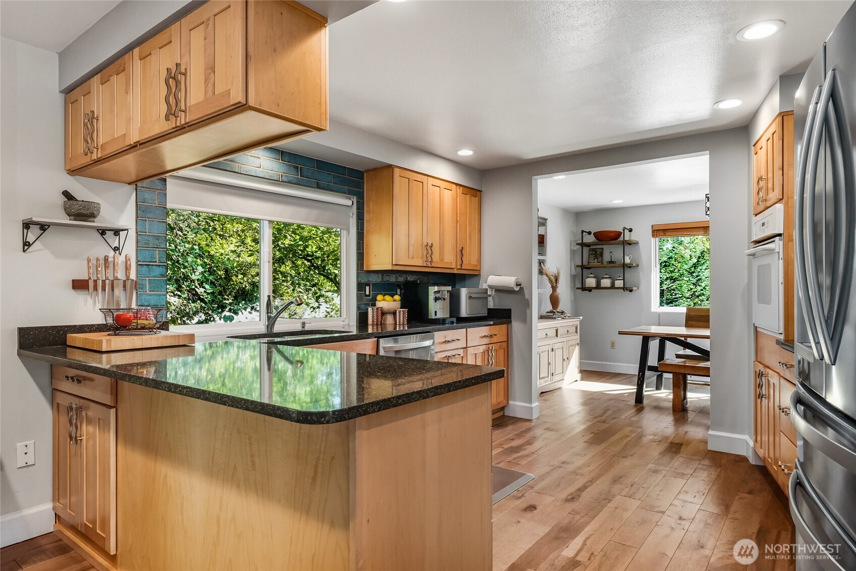 10414 Southwest 110th Street Vashon, WA 98070 - Photo 12 of 37 a kitchen with stainless steel appliances granite countertop a refrigerator a sink dishwasher a stove and a dining table with wooden floor