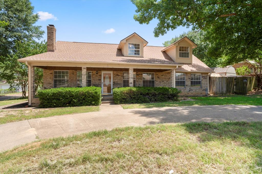 Home with brick siding, a chimney, covered porch, and a shingled roof