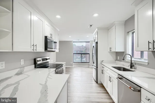 a kitchen with stainless steel appliances granite countertop a sink dishwasher stove and white cabinets with wooden floor