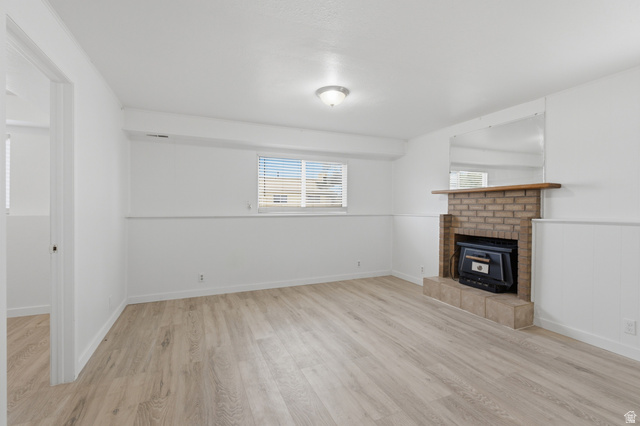 7910 Woolley Way Magna, UT 84044 - Photo 14 of 26 Living area featuring light wood-finish flooring, a brick fireplace with a wood mantle, white paneled walls, and a recessed window with blinds
