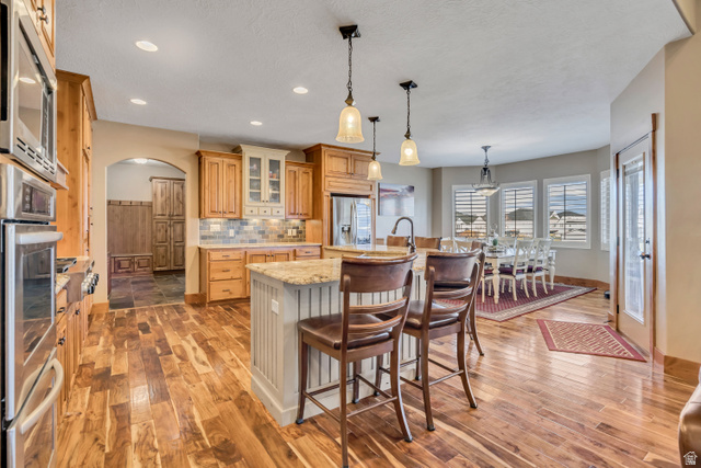 896 West 675 South Mapleton, UT 84664 - Photo 10 of 77 Kitchen with arched walkways, glass insert cabinets, an island with sink, a kitchen breakfast bar, and hanging light fixtures