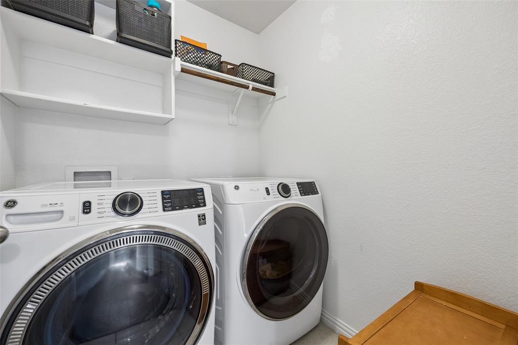 406 Madrone Lane Princeton, TX 75407 - Photo 20 of 30 Dedicated laundry area featuring a white GE front-load washing machine, a matching GE front-load dryer, built-in shelving