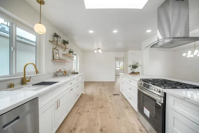 a large kitchen with granite countertop a stove a sink dishwasher and white cabinets with wooden floor