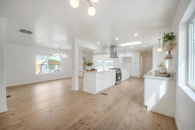 a large white kitchen with kitchen island a sink wooden floor and a large window