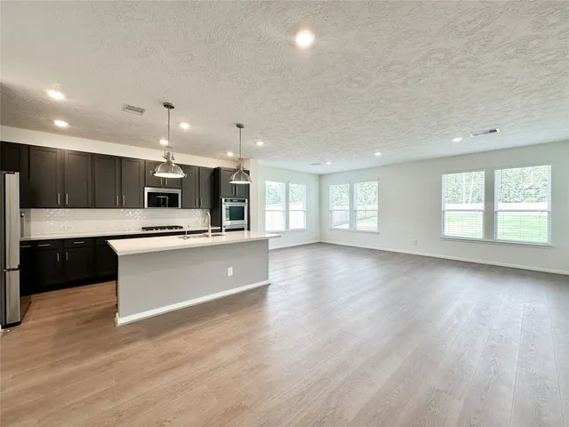 a view of an empty room with kitchen and window