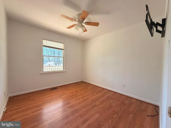 an empty room with wooden floor ceiling fan and windows
