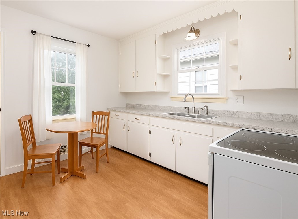 Kitchen featuring open shelves, white electric stove, light countertops, light wood-type flooring, and white cabinets