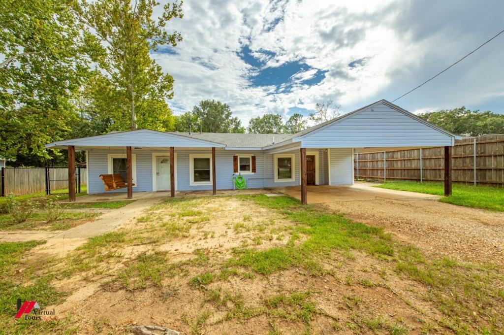 Single story home with dirt driveway, an attached carport, and a patio