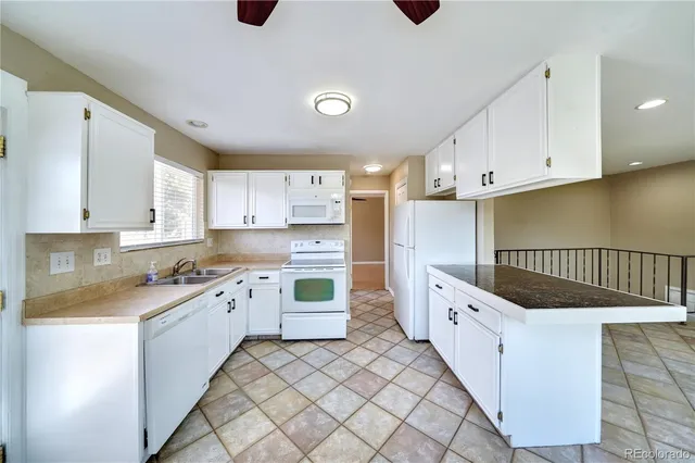 a kitchen with granite countertop a sink and dishwasher a stove top oven with white cabinets