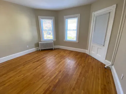 a view of an empty room with wooden floor and a window