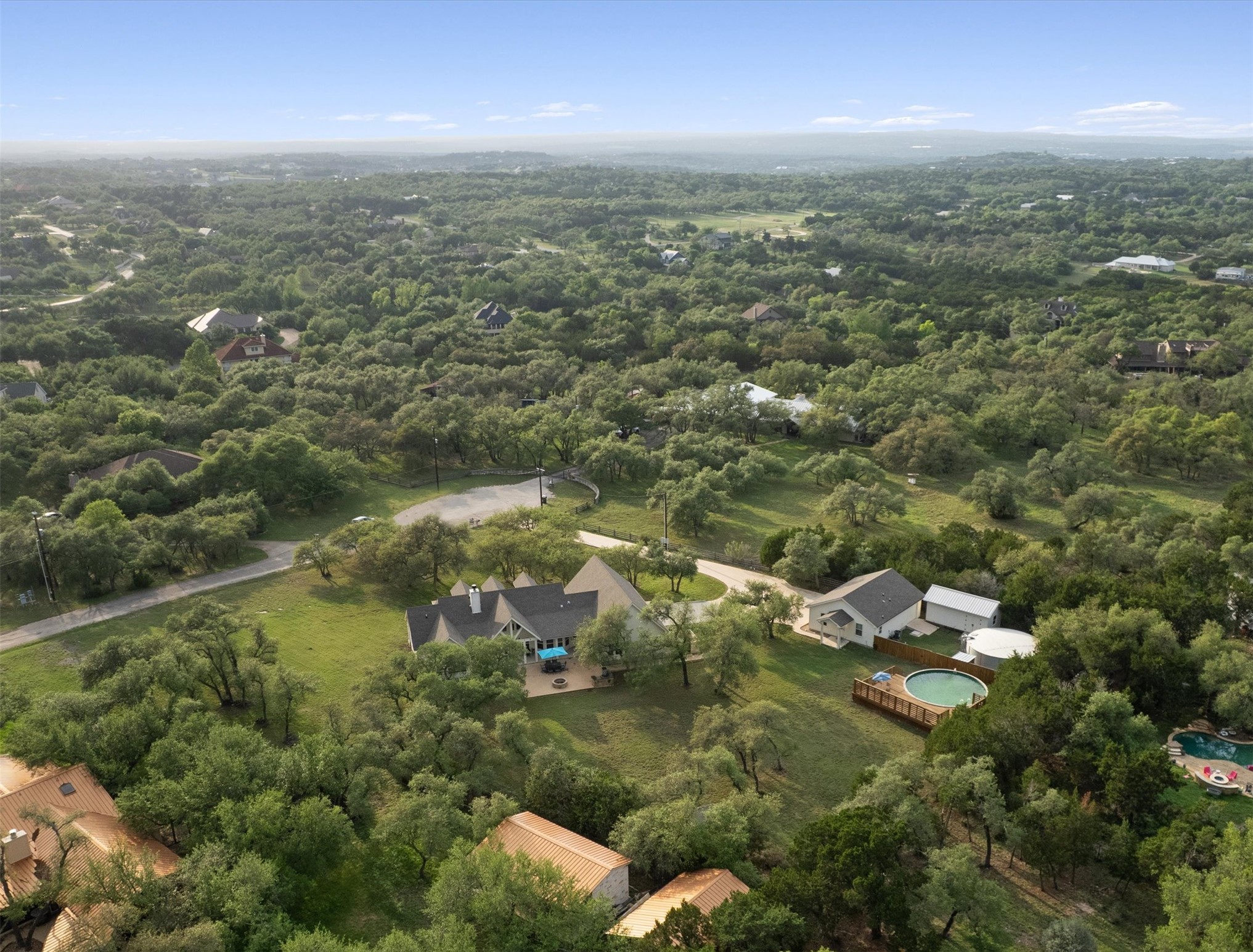 13105 Rooster Springs Road Austin, TX 78737 - Photo 34 of 38 The property is nestled within a lush, tree-filled landscape, featuring a main residence with a covered patio, an additional structure, and a circular above-ground pool with surrounding decking