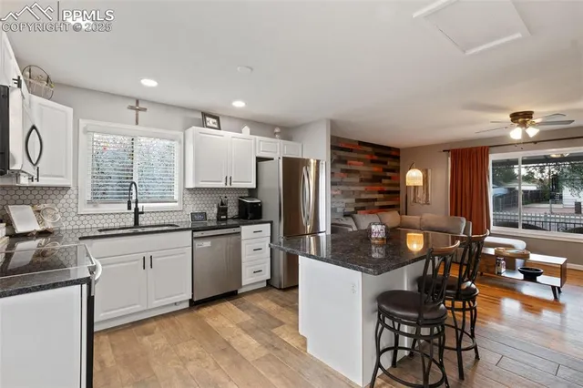 a kitchen with stainless steel appliances granite countertop a stove top oven a sink dishwasher a dining table and chairs with wooden floor