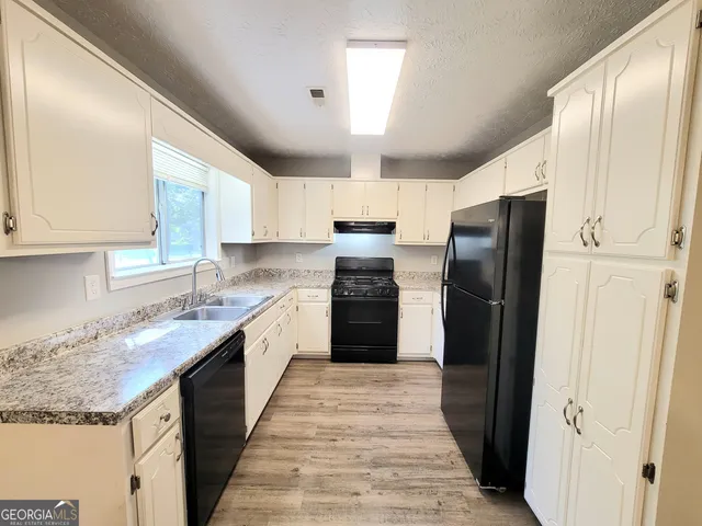 a large kitchen with granite countertop a refrigerator a sink dishwasher a stove and white cabinets with wooden floor