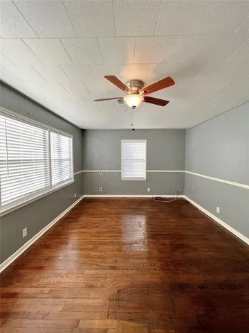 an empty room with wooden floor and windows with curtains