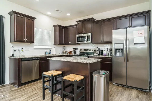 a kitchen with stainless steel appliances granite countertop a refrigerator a stove a sink a dining table and chairs