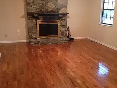 an empty room with wooden floor a fireplace and windows