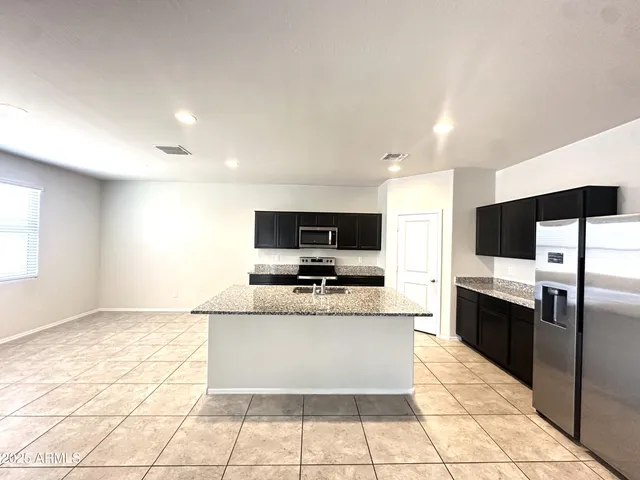 a large kitchen with kitchen island granite countertop a stove top oven a sink a counter top space and cabinets